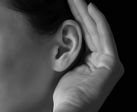 Unrecognizable woman holds her hand near ear and listens, close-upの写真素材