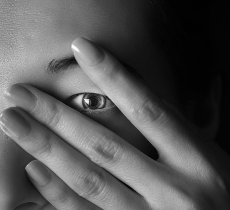 Woman peeks out through her fingers, monochrome imageの写真素材