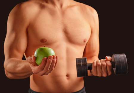 Unrecognizable man holds green apple and dumbbell, concept of healthy lifeの写真素材
