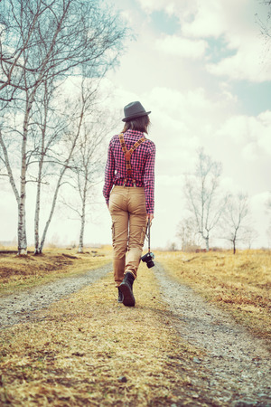 Woman with old photo camera walks on a road in the spring, rear viewの写真素材