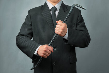 Unrecognizable businessman in a suit holds crowbar, businessman ready to take the businessの写真素材