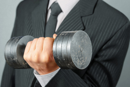 Unrecognizable businessman in a suit holds dumbbellの写真素材