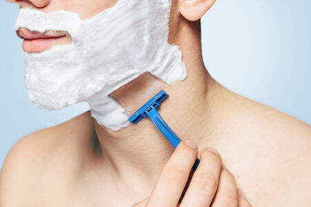 Unrecognizable man with foam on his face is shaving with razorの写真素材