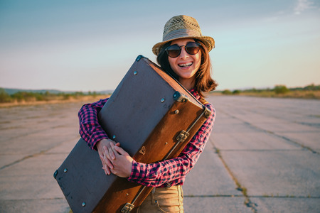 Happy woman traveler embraces a vintage suitcase on roadの写真素材