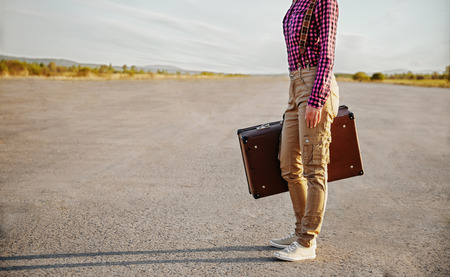 Unrecognizable woman is standing on road with vintage suitcaseの写真素材