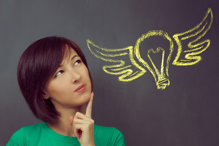 Woman thinks on the background flying light bulb, concept of new idea and inspirationの写真素材