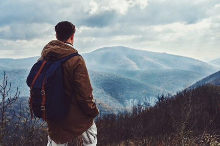 Hiker man with backpack looking at the mountains at autumn season, rear viewの写真素材