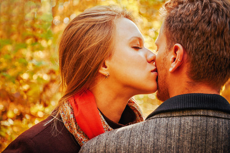 Young beautiful woman with closed eyes kissing a man in autumn parkの写真素材