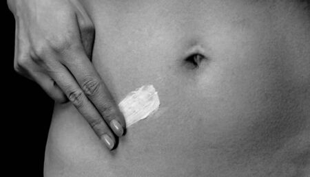Woman applying cream on the belly, close-up, concept of skincare, monochrome imageの写真素材