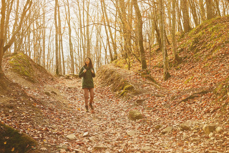 Smiling hiker woman walking in beautiful autumn forest, dry yellow leaves on land. Hiking and leisure theme. Image with sunlight effectのeditorial素材