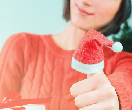 Smiling woman shows thumb up sign, thumb wearing in santa hat. Christmas or New Year celebration