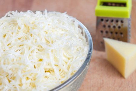 Grated cheese in a bowl, grater, a piece of cheese on a wooden tableの写真素材
