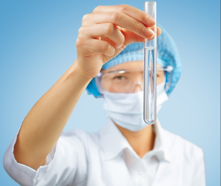 Woman lab technician looks at a test tube of transparent liquidの写真素材