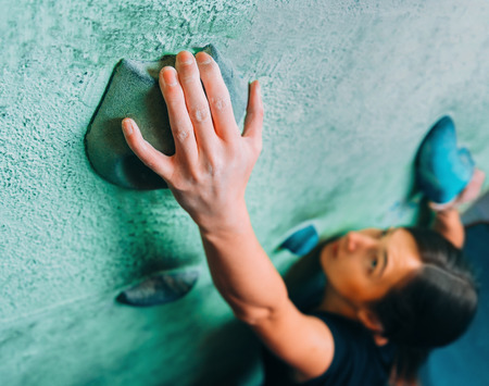 Young woman climbing up on wall in gym, focus on hand