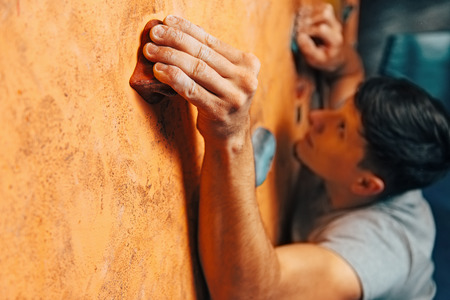 Young man climbing up on wall in gym, focus on handの写真素材