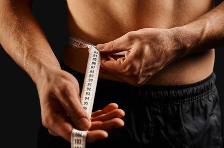 Unrecognizable sportsman measuring waist with centimeter tapeの写真素材