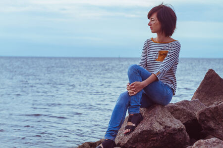 Young woman sitting on a rock by the seaの写真素材