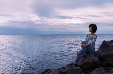 Young woman sitting on a rock by the sea at sunset