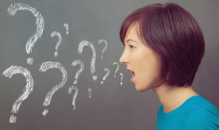 Young woman speaks on the background of blackboard, question marks on the board