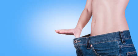 A picture of a young slim woman in oversized pair of blue jeans over blue backgroundの写真素材