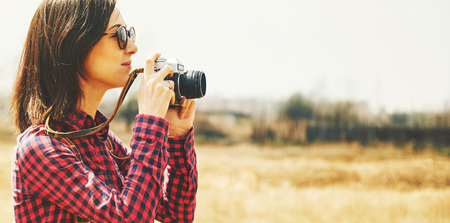 Tourist smiling young woman takes photographs with vintage old photo camera in spring outdoorの写真素材