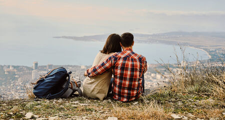 Young couple in love sitting on hill and looking at the city, rear view. Concept of tranquil life...
