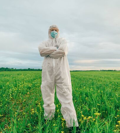 Scientist man in protective uniform standing on summer fieldの写真素材