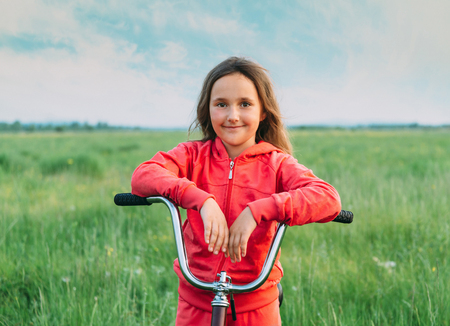 Cheerful little girl with a bicycle on green meadow in summer, healthy lifestyleの写真素材