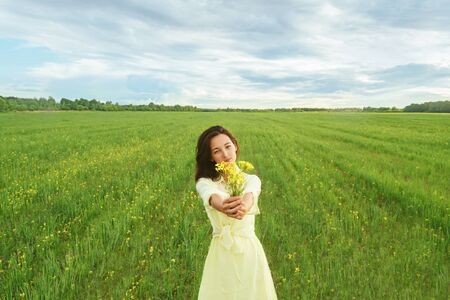Beautiful young woman holding bouquet of yellow flowers on summer meadow