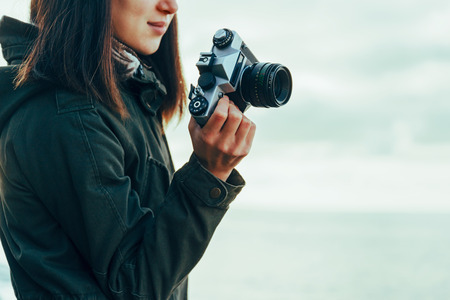 Smiling young woman holding vintage old camera on background of sea. 