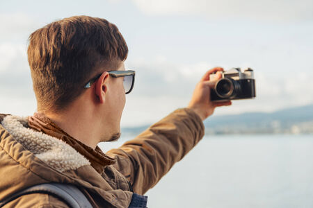 Hiker young man takes photographs self portrait with old photo camera on coastlineの写真素材