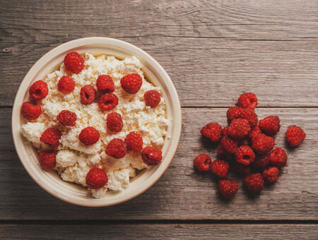 Curd with ripe fresh raspberries in a bowl on wooden background, top viewの写真素材