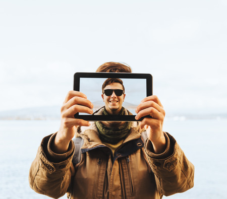 Hiker young man in sunglasses doing a self-portrait with him digital tablet on background of seaの写真素材