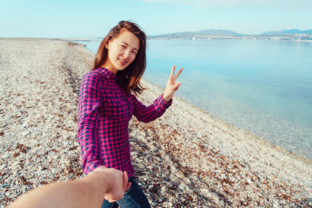 Couple in love. Smiling young woman holding man's hand and showing peace sign on beach near the seaの写真素材