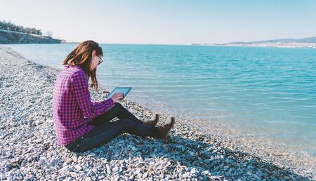 Young woman sitting with digital tablet on beach near the sea