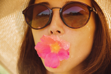 Portrait of beautiful woman in sunglasses and hat with wide brim with pink flower, concept of happiness and summer moodの写真素材