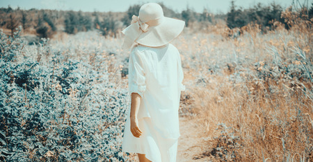 Young woman in dress and hat with wide brim walking in summer fairy beautiful park, rear viewの写真素材
