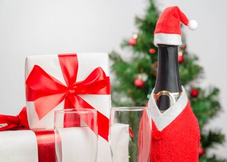 Gift box with red ribbon, a bottle of champagne on the background of Christmas treeの写真素材