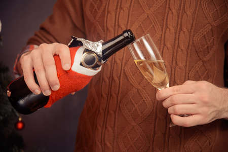 Unrecognizable man in sweater is pouring champagne into a glass