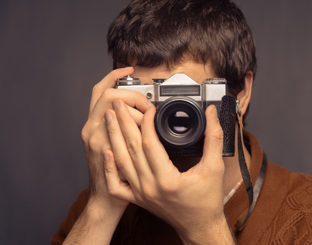 Young man is holding a vintage photo cameraの写真素材