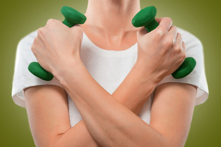 Woman holds dumbbells, arms crossed, face is not visibleの写真素材