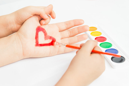 Child paints red heart on the hand, face is not visibleの写真素材
