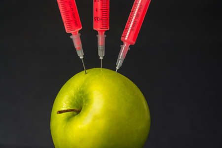 Red liquid in the syringe injected into apple on a black , close-upの写真素材