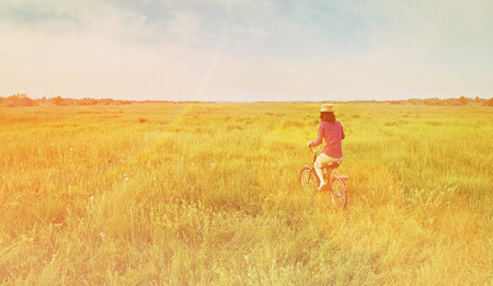 Hipster girl is cycling on green meadow in summer. Image with sunlight effectの写真素材