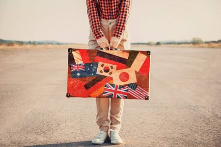 Traveler woman with a suitcase standing on road. Suitcase with stamps flags of different countryの写真素材