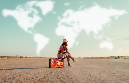 Traveler woman sitting on a suitcase and dreaming about adventures. Map of the world is painted in sky. Concept of travel Traveler woman sitting on a suitcase and dreaming about adventures. Map of the world is painted in sky. Concept of travel