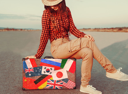 Traveler young woman sitting on suitcase. Suitcase with stamps flags of different countries. Concept of travelの写真素材