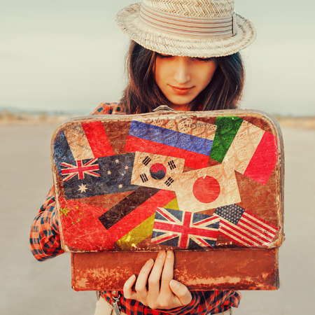 Young beautiful woman looking for something in the open suitcase. Suitcase with stamps flags of different countries. Concept of travelの写真素材