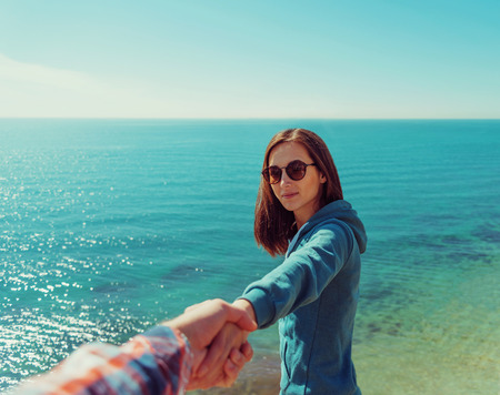 Couple in love resting on coastline near the sea in summer. Beautiful young woman holding hand her boyfriend. Point of view shotの写真素材