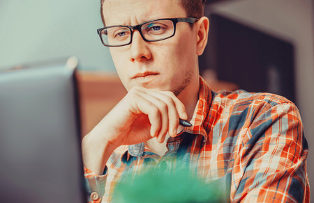 Pensive young man working over laptop in the officeの写真素材